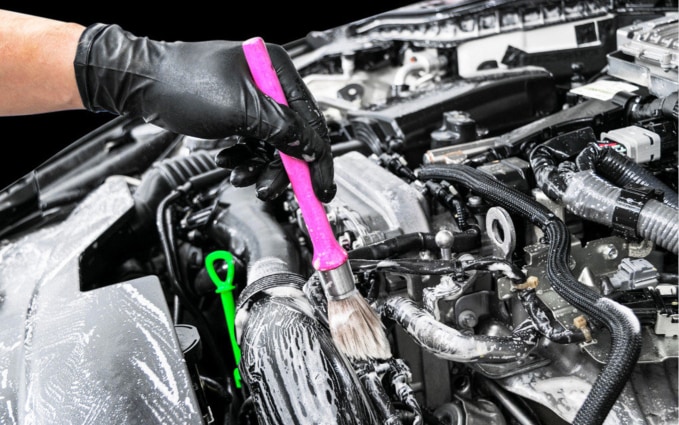 Close-up of gloved hands detailing a car engine with a brush.