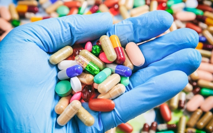 Close-up of a gloved hand holding assorted pills. Nitrile gloves are used in many medical settings.