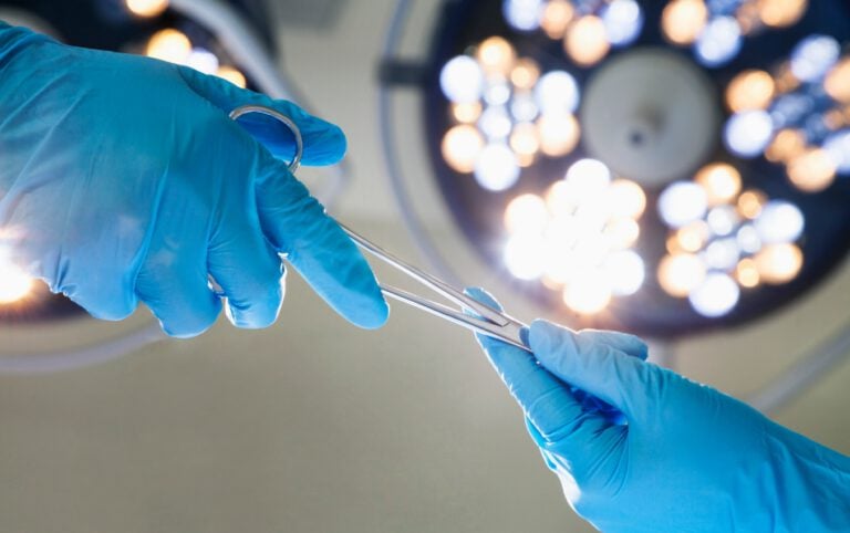 Surgeons' gloved hands exchange surgical scissors in an operating room.