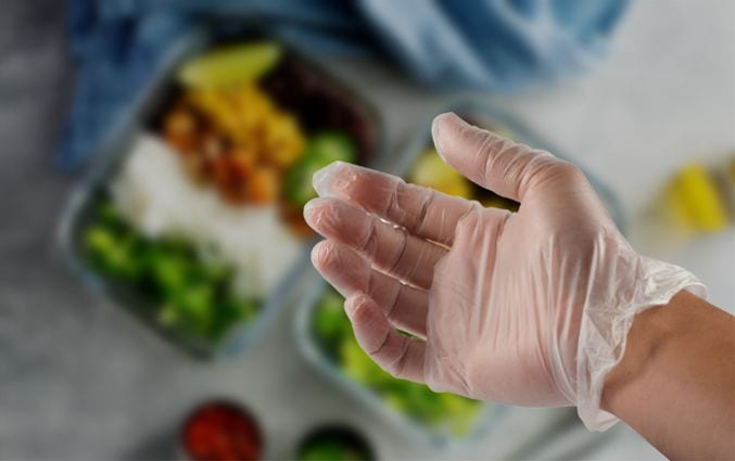 Close-up of hand wearing clear vinyl food-safe gloves.