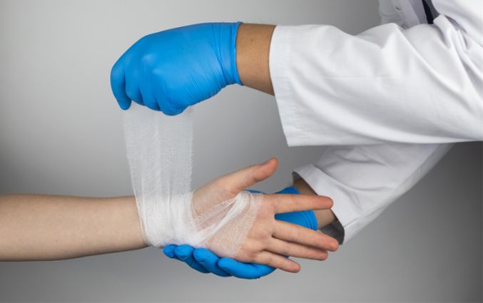 Doctor's hands in blue nitrile gloves bandaging a patient's wrist.