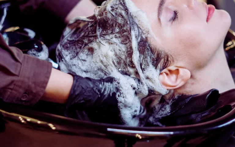 Hairdresser wearing disposable nitrile gloves washes client's hair.