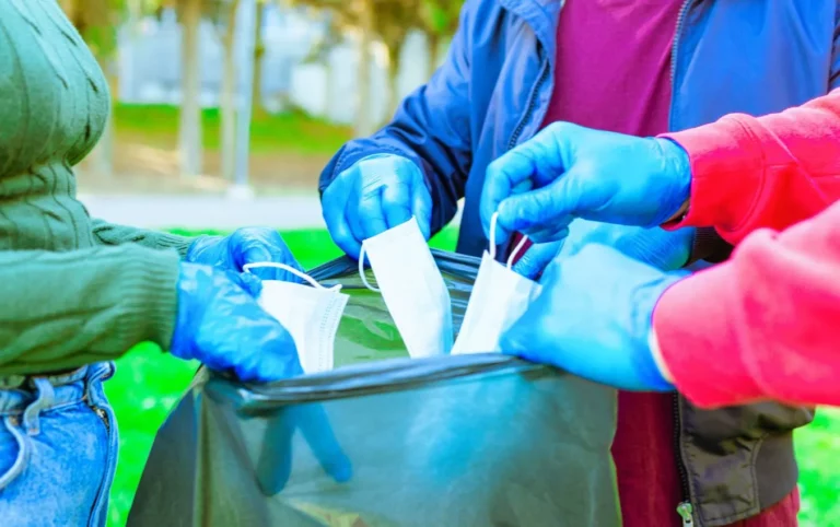 People in nitrile gloves responsibly dispose of used face masks into a trash bag.