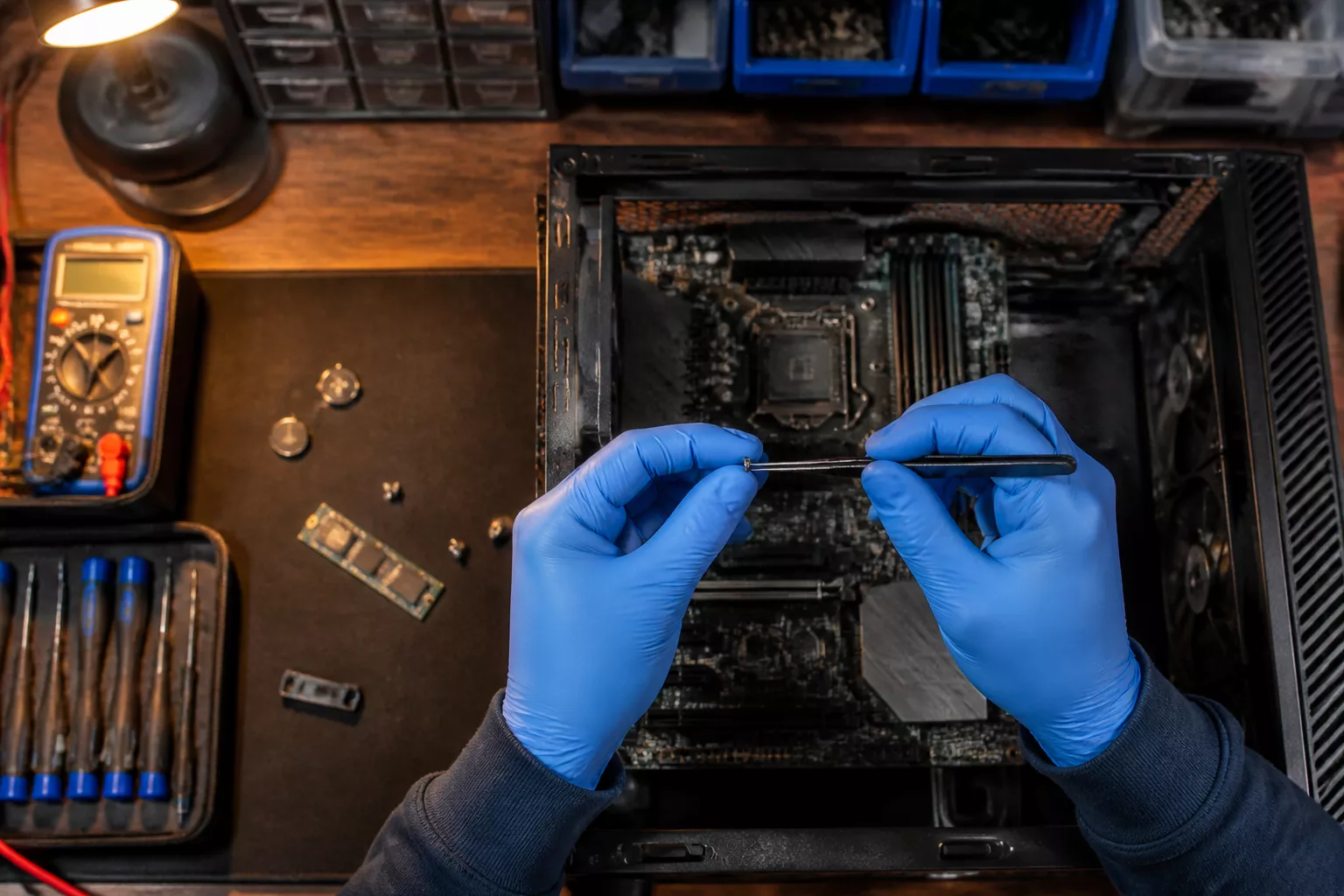 () detailed photograph showing a technician's workbench from overhead perspective, blue nitrile gloved hands holding a tiny